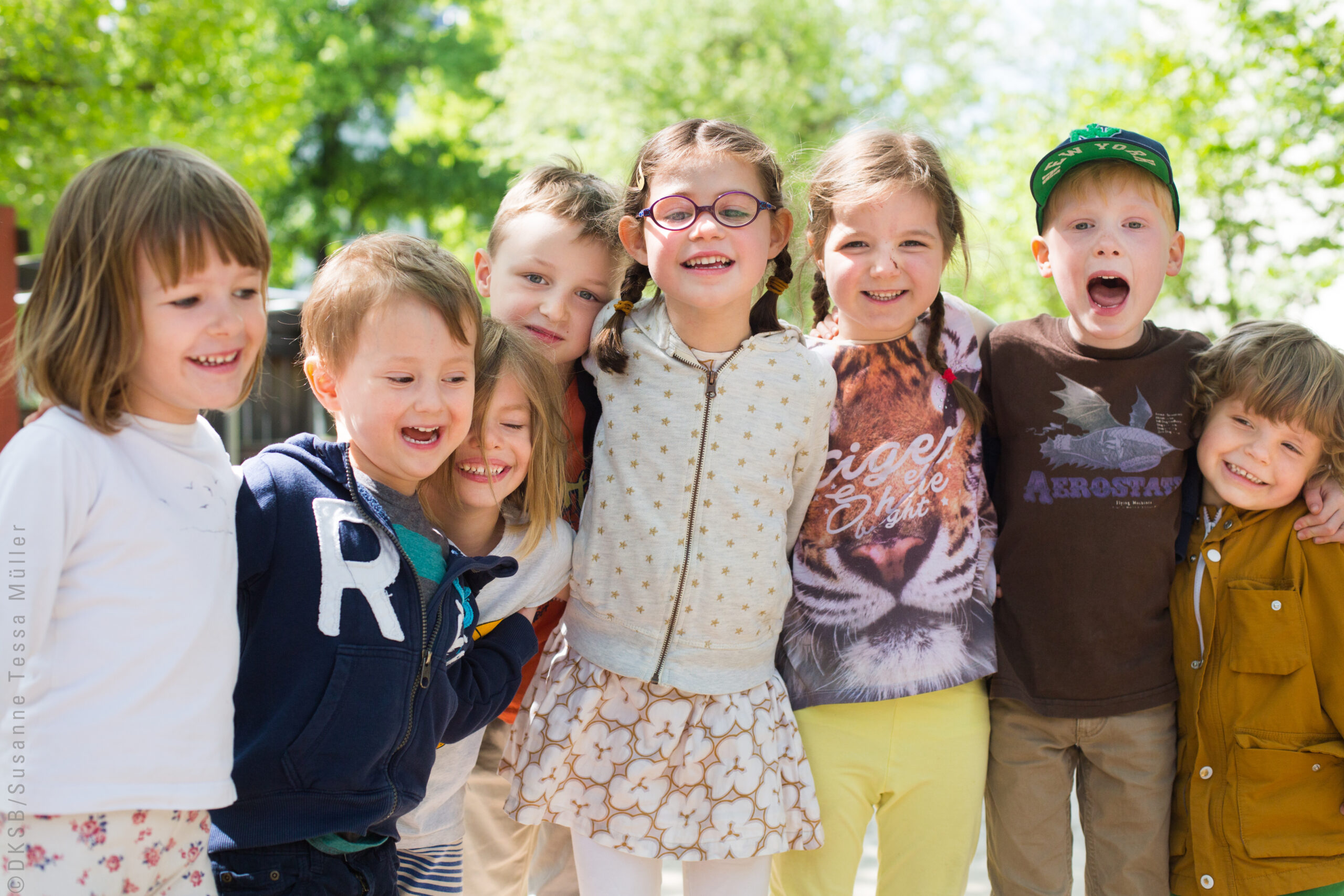 Kinder umarmen sich und lachen freundlich in die Kamera